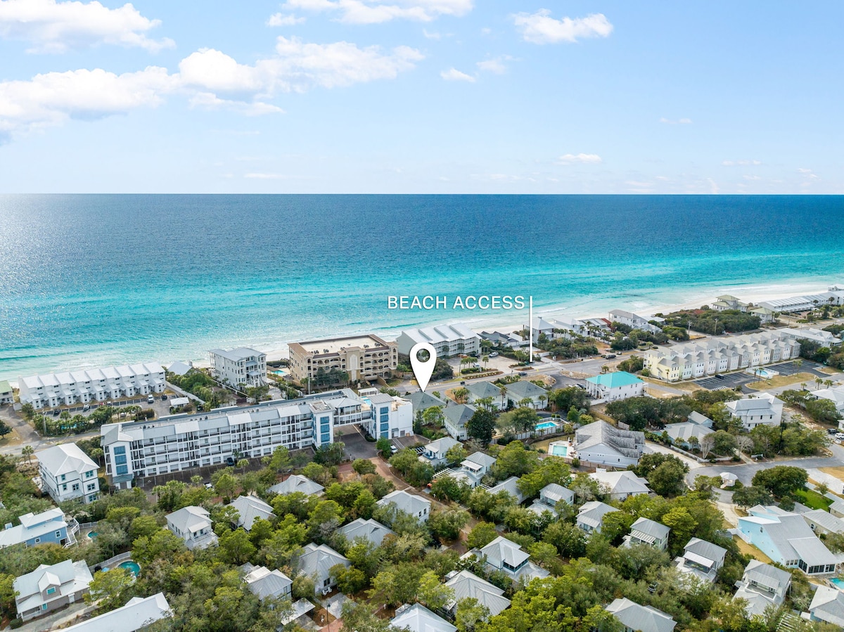 An aerial view captures the scenic coastline and the proximity to public beach access. The vibrant blue waters meet the sandy shore, while clusters of coastal homes are positioned nearby, illustrating the inviting atmosphere of the community.