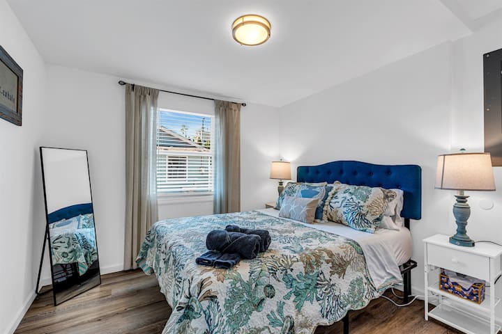 Bedroom one with a queen bed, navy tufted headboard and coastal reef-print bedding
