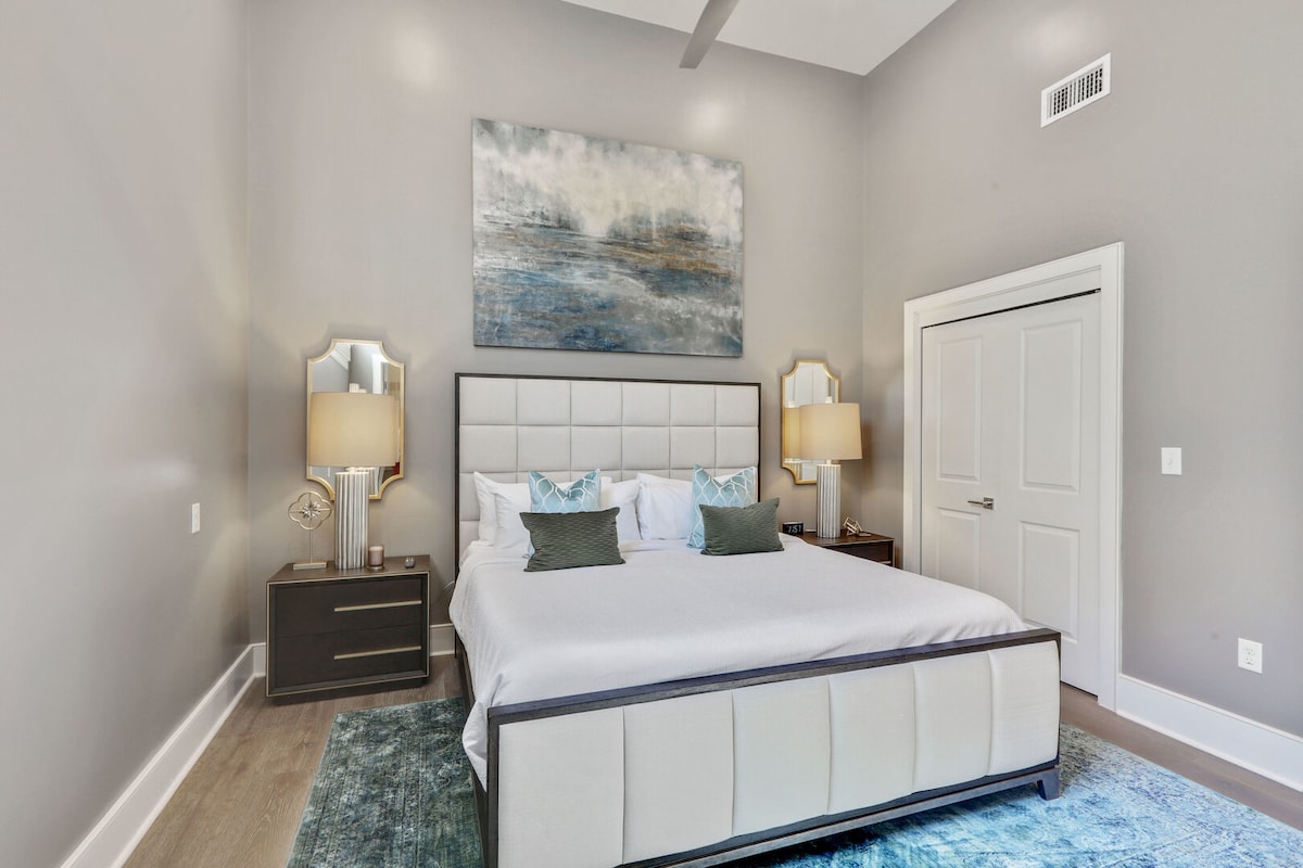 חדר שינה ראשי מרווח עם מיטה זוגית גדולה, חדר רחצה צמוד וארונות מעצבים. כולל שידות לילה, מנורות, קולבים, מתלים למזוודות, שעון מעורר, מכונת רעש לבן וטלוויזיית Samsung Smart 4K בגודל 50אינץ 'עם אפליקציות סטרימינג ו - DIRECTV Entertainment.