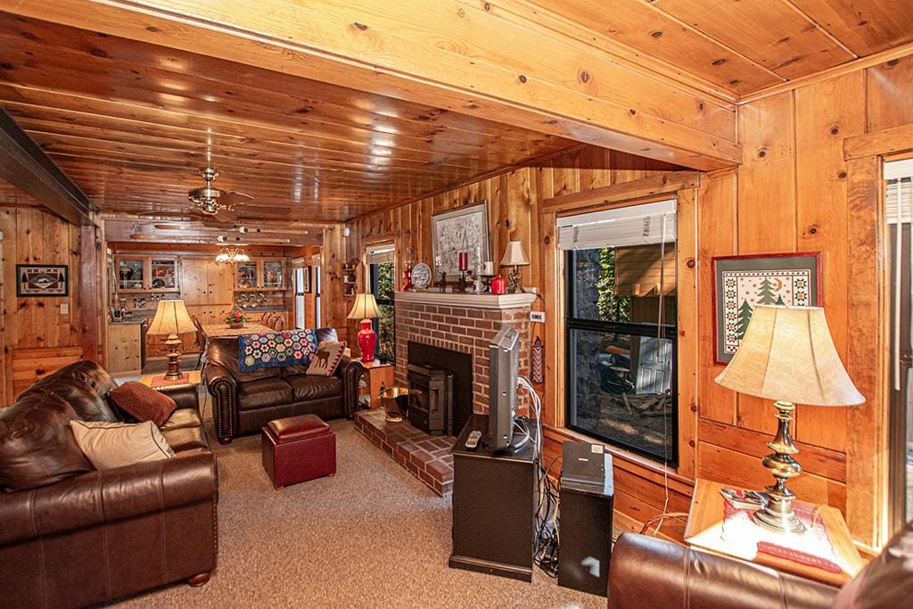 The living room features wooden paneling and a ceiling with exposed beams. Two leather sofas are positioned around a brick fireplace, complemented by lamps and decorative accents. Natural light enters through the windows, illuminating the cozy atmosphere.