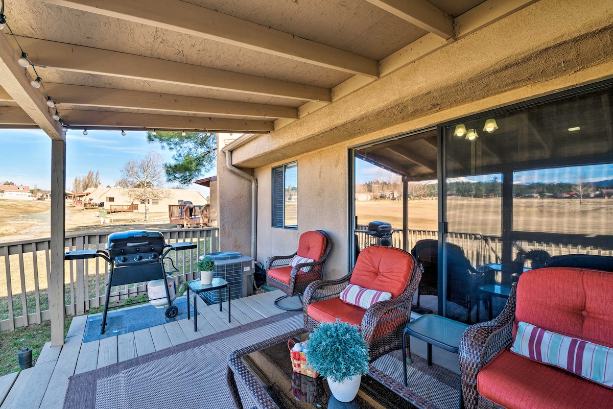 An outdoor deck area features comfortable seating, including two wicker chairs with cushions and a glass-topped coffee table. A gas grill stands nearby, and the space offers views of the golf course and surrounding mountains with ample sunlight filtering through.
