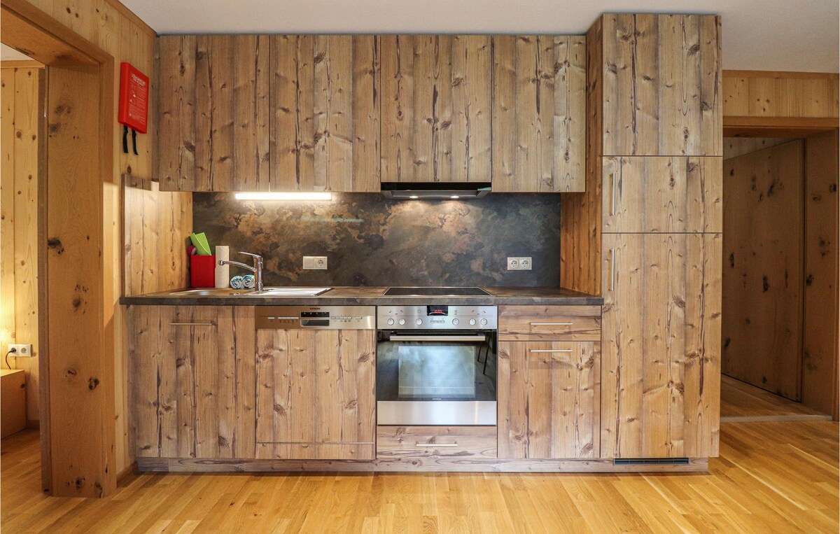 A modern kitchen area features wooden cabinetry and a stone countertop. Appliances, including an oven and a dishwasher, are integrated into the cabinetry. Under-cabinet lighting creates a subtle glow, enhancing the warm wood tones and inviting atmosphere of the space.