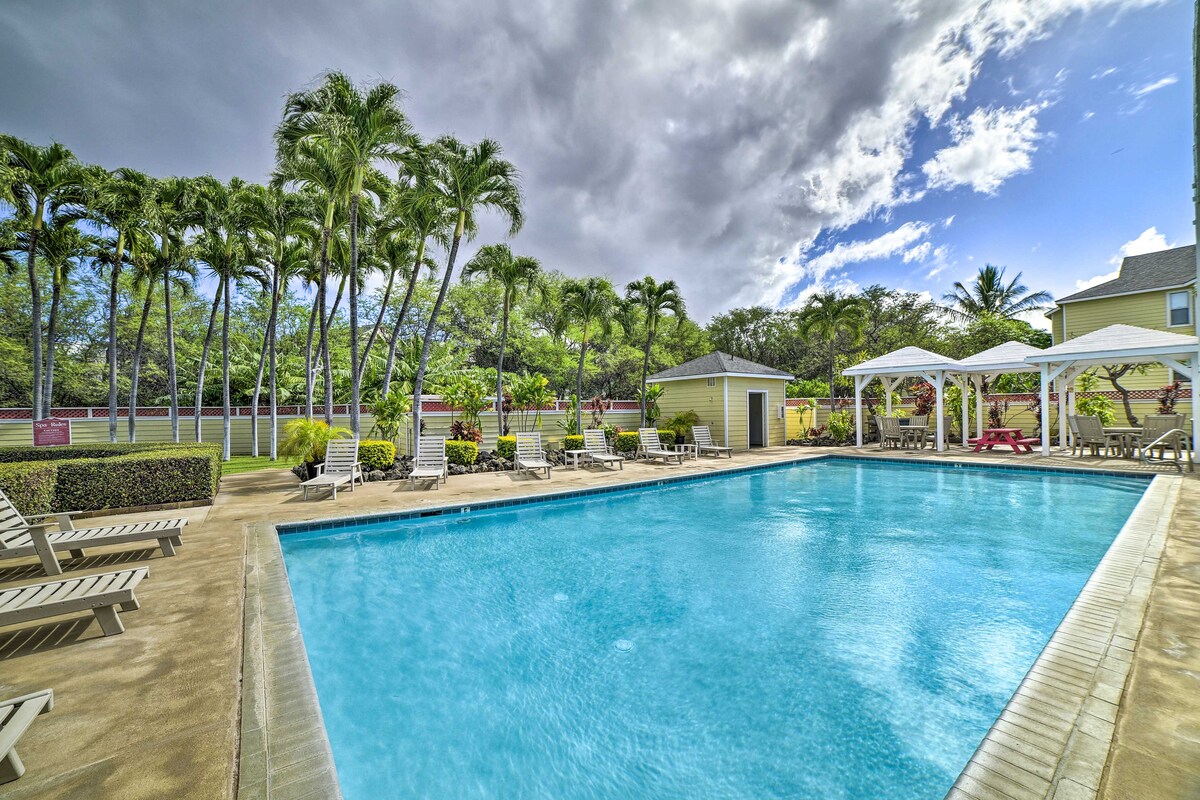 A large outdoor pool is surrounded by palm trees and well-maintained landscaping. A shaded gazebo and lounge chairs are positioned nearby, providing spaces for relaxation. The pool's clear water reflects the bright sky, enhancing the inviting atmosphere of the communal area.