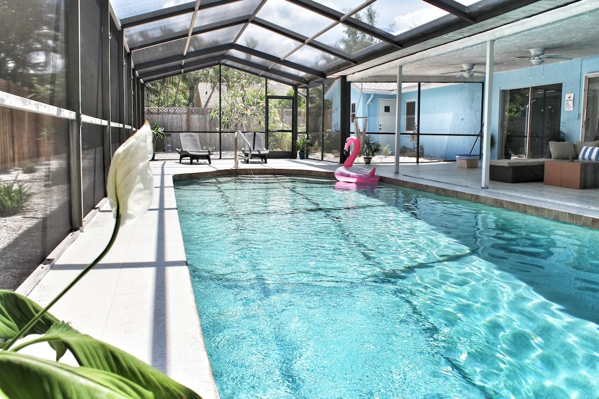 A private heated pool is surrounded by a screened enclosure, offering a clear view of the shimmering water. A large lounge chair sits on one side, while a pink inflatable float adds a pop of color to the serene setting. Lush greenery is visible around the pool area.