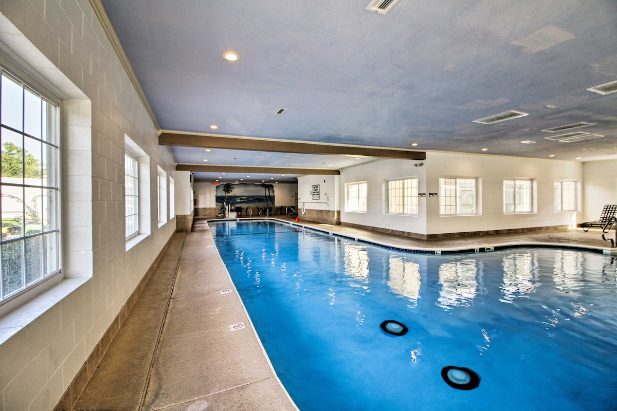 An indoor swimming pool is seen, featuring a smooth, blue surface reflecting soft overhead lighting. The pool is flanked by large windows that allow natural light to brighten the space, enhancing the overall ambiance.