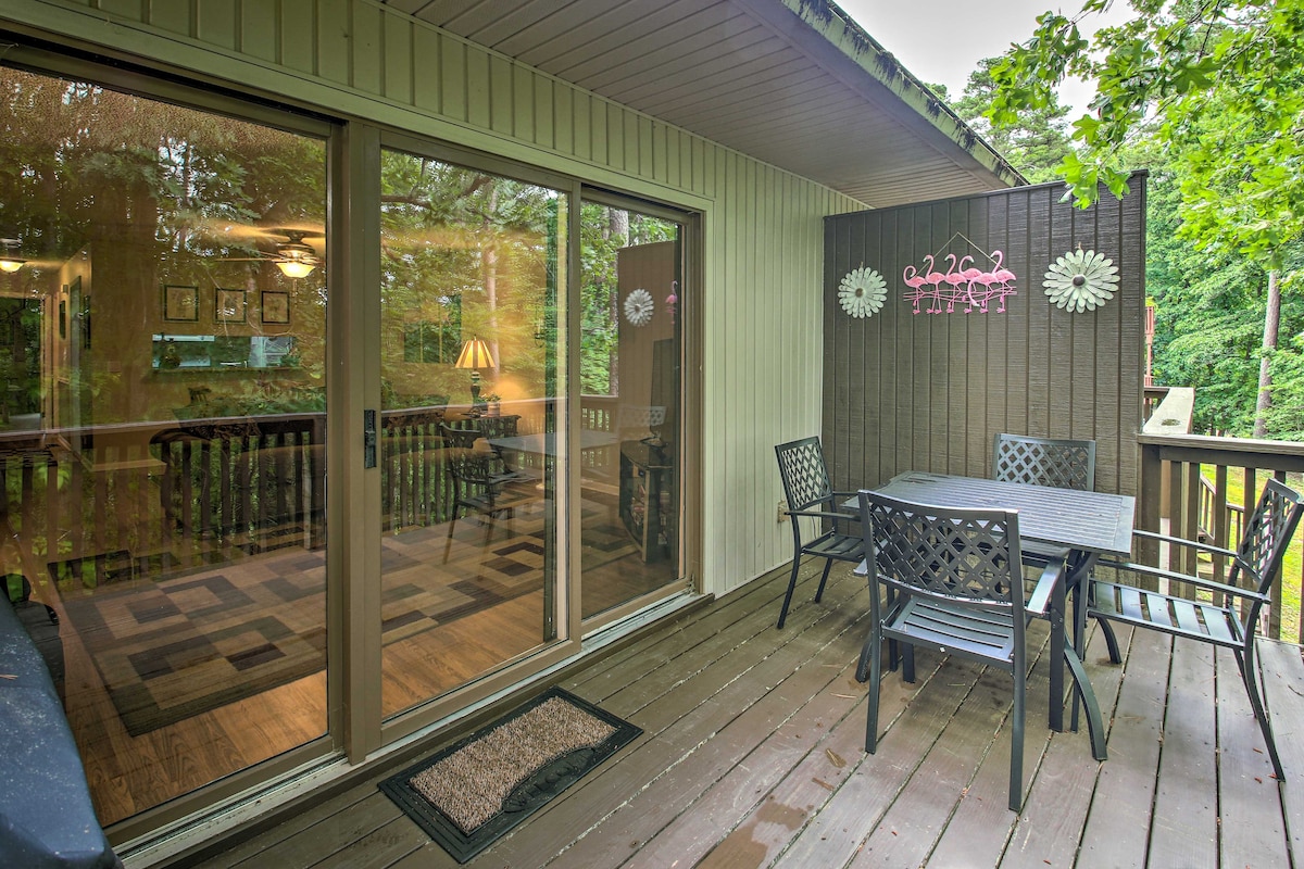 A partially-covered deck features outdoor seating arranged around a table, complemented by a propane grill nearby. Sliding glass doors reflect a view of the interior, while surrounding trees create a natural backdrop, enhancing the serene outdoor setting.