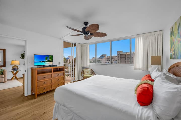 Dormitorio con sábanas blancas y frescas, detalles en rojo intenso y amplias ventanas que se abren a un paisaje urbano.