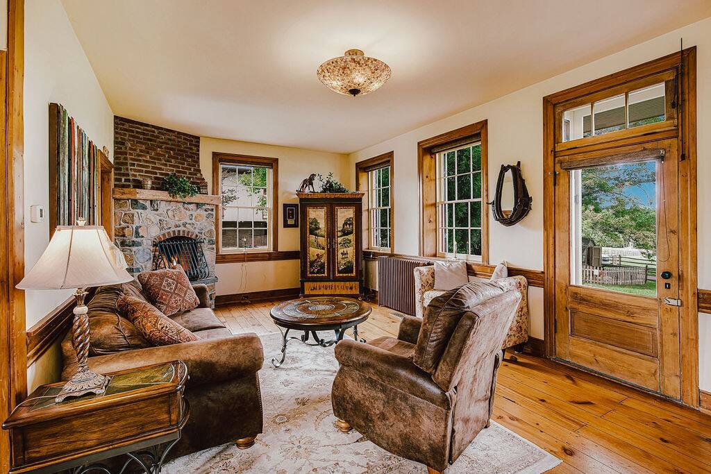 A comfortable living area features a mix of plush seating, including a loveseat and armchair, arranged around a decorative round coffee table. A stone fireplace adds a focal point, while large windows provide natural light and reveal views of the surroundings.