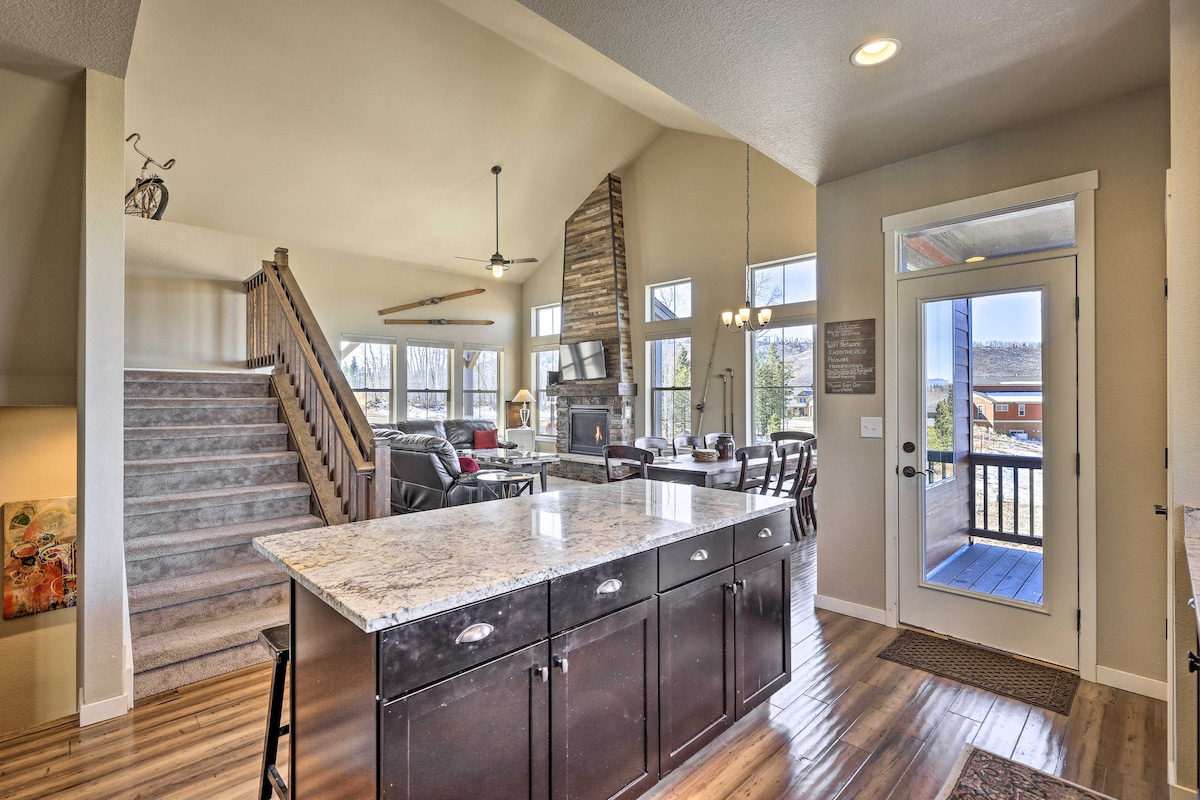 A spacious kitchen area features a large island with granite countertops and dark cabinetry. The room showcases an open-plan design with views of the living area and dining space, illuminated by natural light from large windows. Stairs lead to an upper level.
