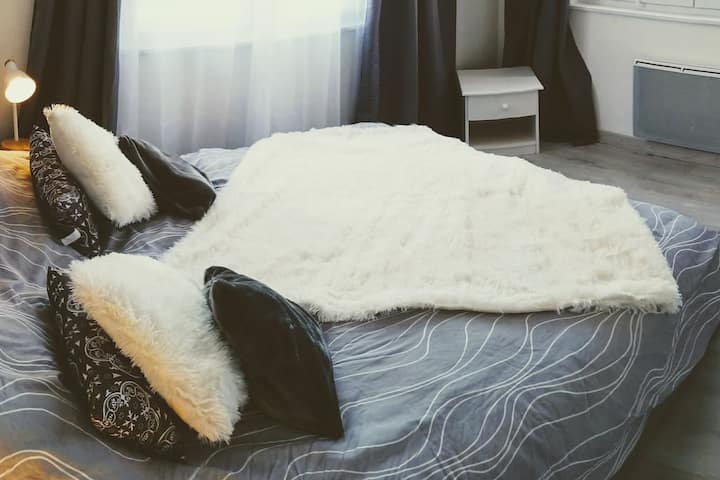 Kitanda kikubwa cha mtu mmoja chenye blanketi laini na mto wa manyoya, meza ya kando ya kitanda na mapazia ya kuzuia mwanga kwa ajili ya usiku wenye utulivu