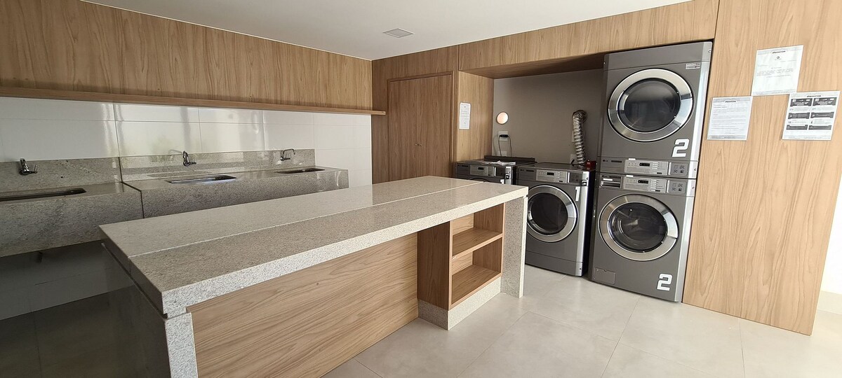 A functional laundry room features modern machines for washing and drying clothes. A large countertop is available for folding and organizing laundry. The space is well-lit with neutral tones, enhancing the clean and practical atmosphere.