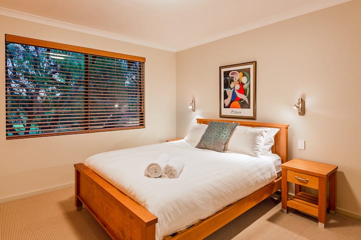 在标准双人床尺寸的第二间卧室享受宁静的夜晚，配有宁静的艺术品、大窗户和宁静的花园景观。