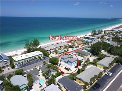 An aerial view of the surrounding area showcases the proximity to the beach, with the Gulf's clear waters and sandy shore visible in the background. Nearby structures, including residential homes and parking areas, are positioned around the location labeled 'Beach Access.'