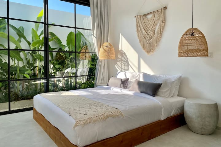 Large arched glass doors connect the bedroom seamlessly to the outdoors. Light flows freely, enhancing the room’s tranquil and airy character.