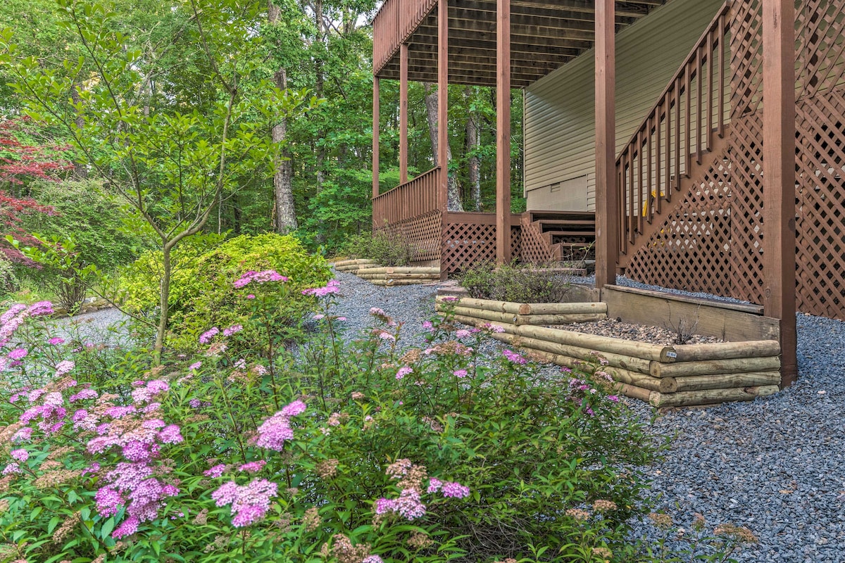 A gravel pathway leads to the entrance of the downstairs unit, surrounded by vibrant flowering plants. A covered deck is visible above, supported by wooden beams, providing a shaded outdoor area for relaxation.