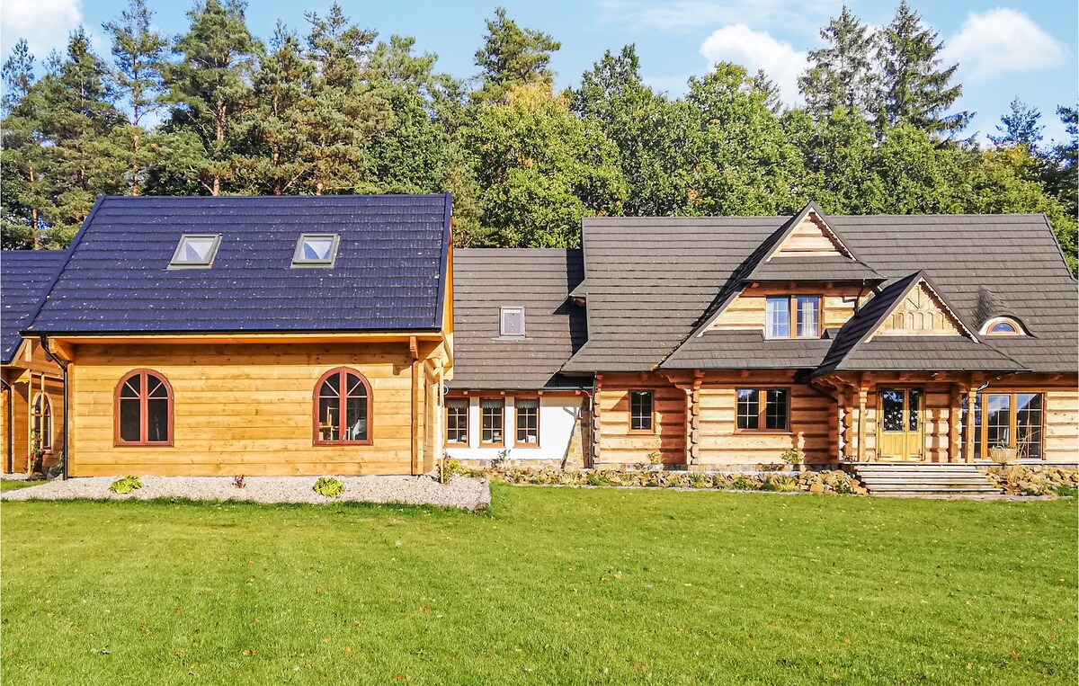 A spacious wooden holiday home features a blend of traditional and contemporary architecture. The exterior is adorned with natural wood, large windows, and a welcoming entryway. Lush green grass surrounds the structure, creating an inviting outdoor space amidst a backdrop of trees.