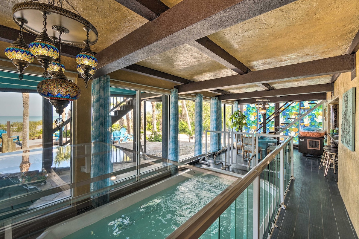 An indoor pool is featured, surrounded by elegant decor and large windows offering views of the beach. Ornate hanging lanterns add a decorative touch, while a staircase leads to additional outdoor spaces, integrating luxurious comfort with scenic oceanfront accessibility.