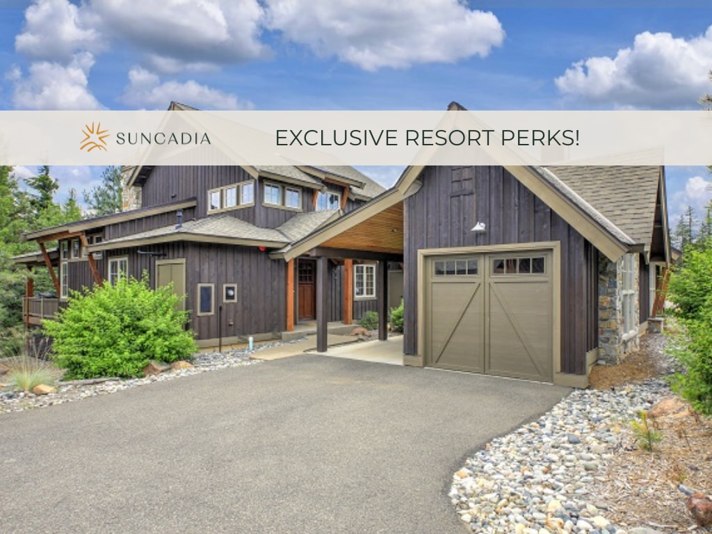 A modern, two-story townhome is presented, featuring a combination of dark wood and stone accents. The front entry is highlighted by a covered porch and an attached garage. Lush greenery and decorative stones enhance the inviting landscape, creating a welcoming entrance.