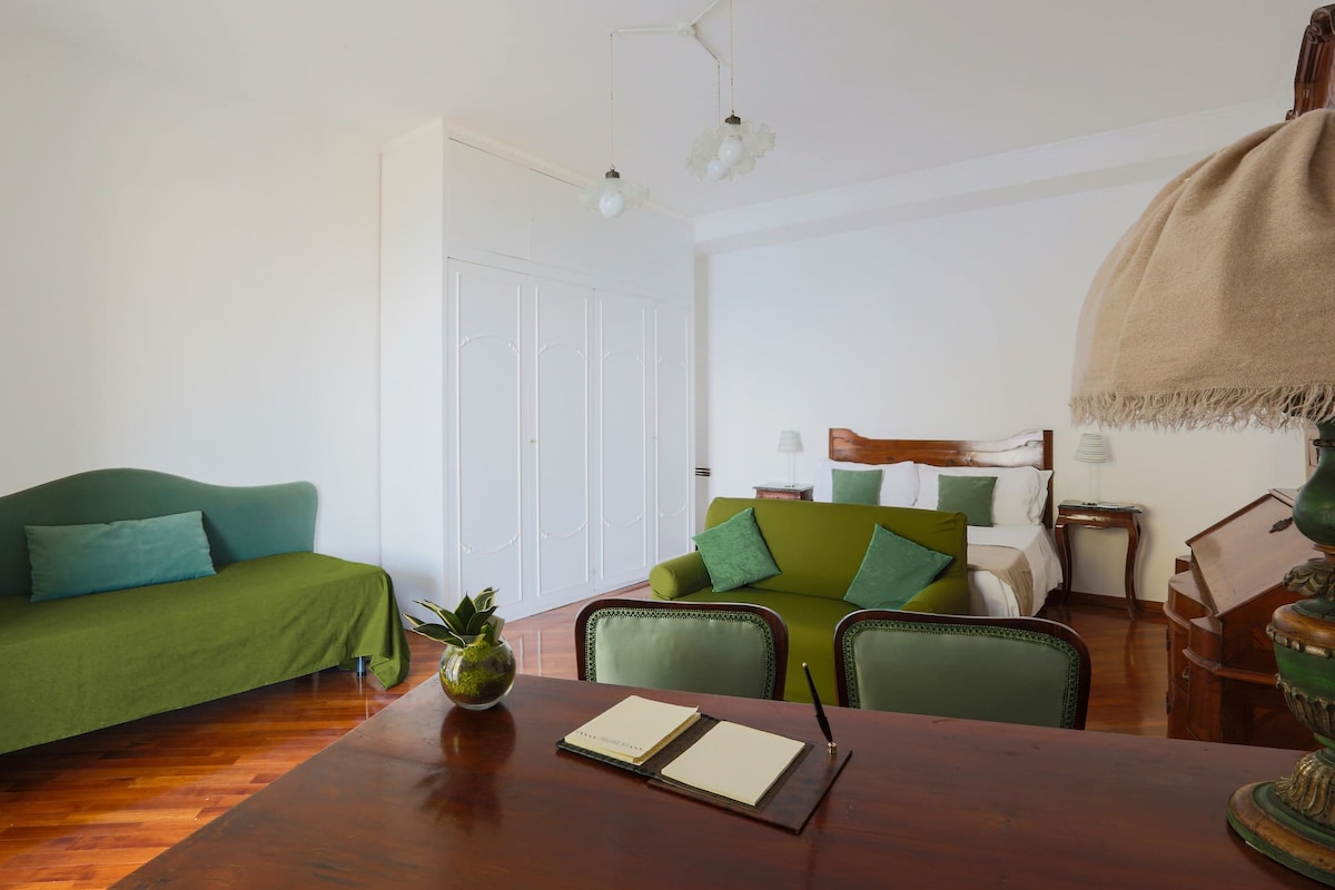 غرفة نوم بسرير بحجم كينغ وسرير مفرد واحد مع ملاءات بياضات جديدة ومساحة عمل مع مكتب وكرسي وأريكة وطاولات بجانب السرير مع مصابيح وخزانة ملابس وتكييف هواء وإمكانية الوصول المباشر إلى شرفة خاصة مع طاولة وكراسي مع دش.