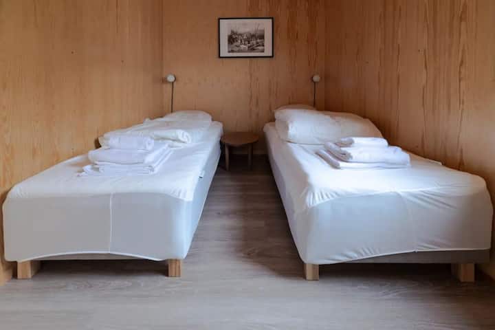Dormitorio minimalista con dos camas individuales, sábanas blancas y paredes con paneles de madera natural.