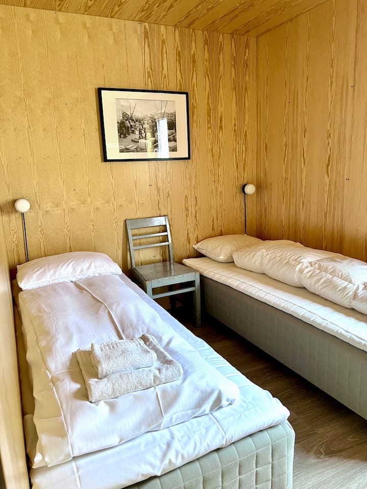 Acogedor dormitorio con dos camas individuales, paredes de madera y decoración minimalista para un ambiente cálido y acogedor.