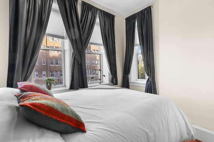 Bright and airy room featuring queen size bed with curtained windows and blinds