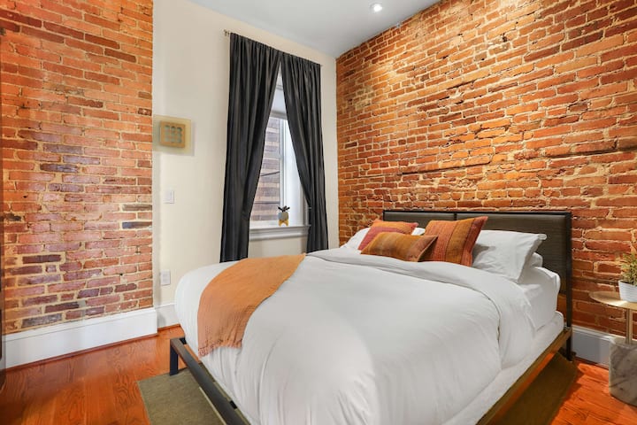 Bright and comfortable bedroom with timeless brick details, queen size bed and plush pillows