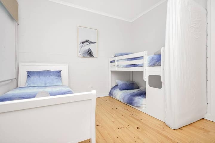 Une chambre lumineuse avec un lit simple et un lit superposé, décorée dans des tons bleus doux pour une ambiance côtière décontractée.