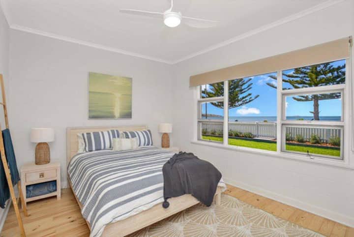 Chambre principale avec un lit queen size encadré par de grandes fenêtres donnant sur la pelouse luxuriante et la vue sur l'eau.