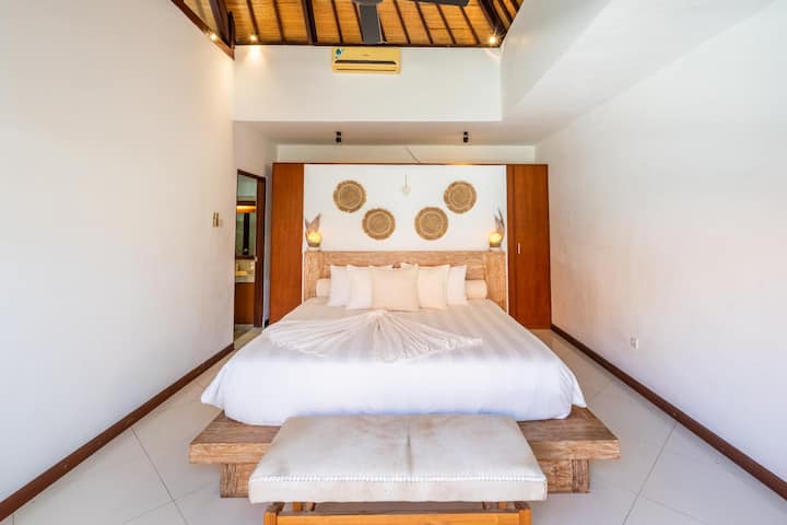 El dormitorio principal de Villa Jiwa ofrece una lujosa cama tamaño king, un elegante baño privado con bañera, un tocador y vistas serenas a la piscina cristalina.