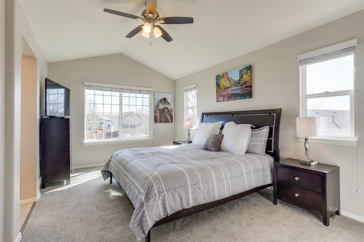 A well-appointed master bedroom features a spacious bed with neatly arranged pillows and a soft, textured blanket. Two bedside tables with lamps flank the bed, and a dresser is positioned nearby. Natural light fills the room through large windows, highlighting serene wall art.