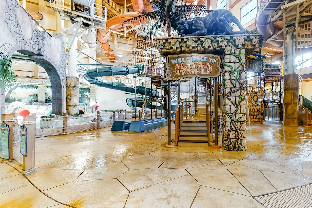 A vibrant indoor water park area is depicted, featuring large water slides and a decorative jungle theme. A welcoming entrance marked 'Welcome to Temple' leads into the space. Smooth concrete flooring extends throughout, bordered by colorful water attractions and structures designed for family fun.