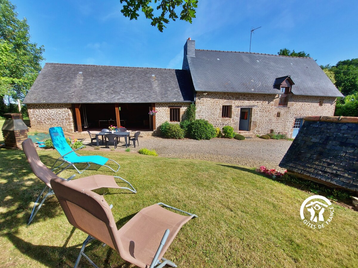 A stone cottage from the 18th century is surrounded by a landscaped garden and gravel patio. Equipped with outdoor seating, a dining table, and a barbecue area, the setting invites relaxation. Clear blue skies and greenery are prominent, providing a calm and open atmosphere.