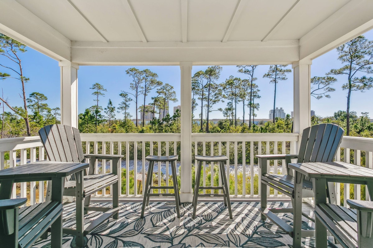 A private balcony with four wooden chairs and two matching stools is set against a backdrop of trees and serene natural views. The space is enhanced with a patterned outdoor rug, providing a cozy area to relax and enjoy the surrounding environment.