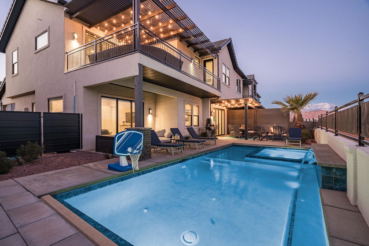 An outdoor space showcases a private swimming pool with a hot tub adjacent to it. Comfortable lounge chairs are positioned around the pool, while a covered patio area features dining seating and soft lighting above. A basketball hoop stands nearby, enhancing the recreational appeal.