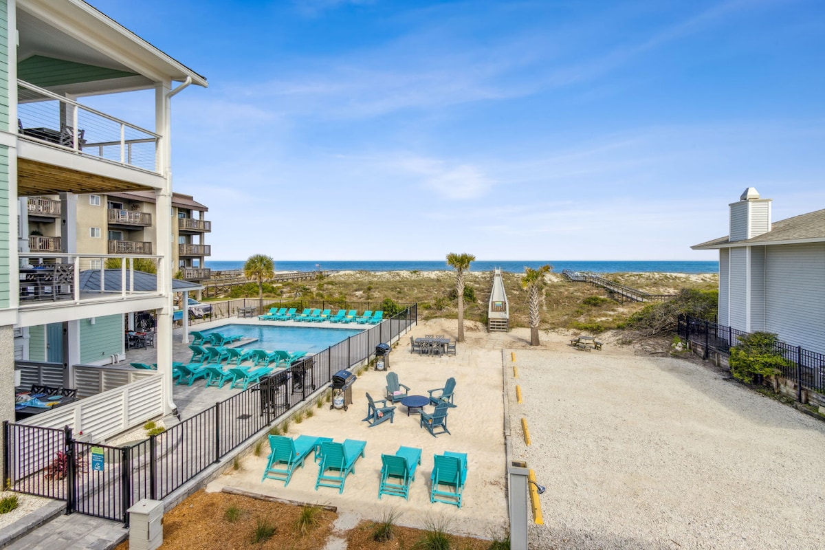 The outdoor space features multiple lounging chairs and a dining area, providing a relaxing atmosphere with ocean views. A beach walkover leads directly to the shoreline, while well-maintained landscaping surrounds the area, enhancing the coastal setting.