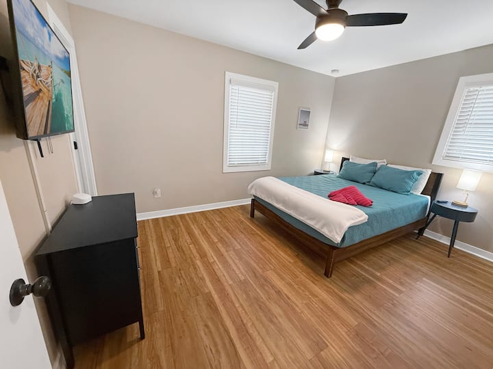 Queen guest bedroom with smart TV, wood floors, and bedside lighting.