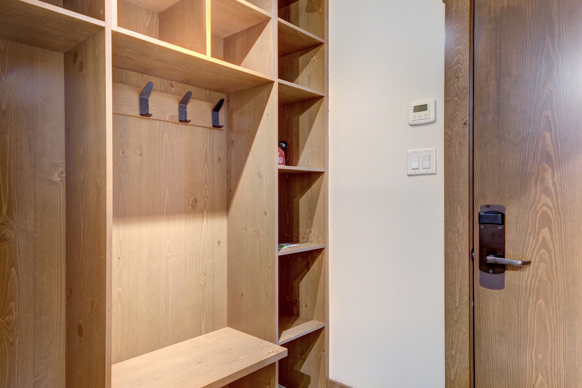 A spacious storage area is designed with wooden shelving and hooks for organization. The warm finish of the wood adds a natural feel, while a door with a simple handle leads to the rest of the accommodation, offering convenience for guests.