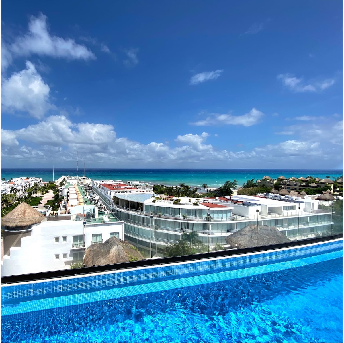 A panoramic view showcases the vibrant coastline with turquoise waters and lush greenery. The image captures the serene infinity pool edge, seamlessly blending with the sky and ocean, inviting relaxation and visual tranquility.