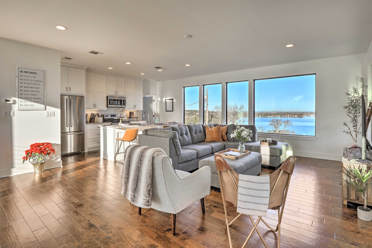 A modern living space features large windows that provide views of Granbury Lake. Sleek furnishings include a sectional sofa, an armchair, and a small table. Light wood floors are complemented by neutral walls, enhancing the bright and open atmosphere.