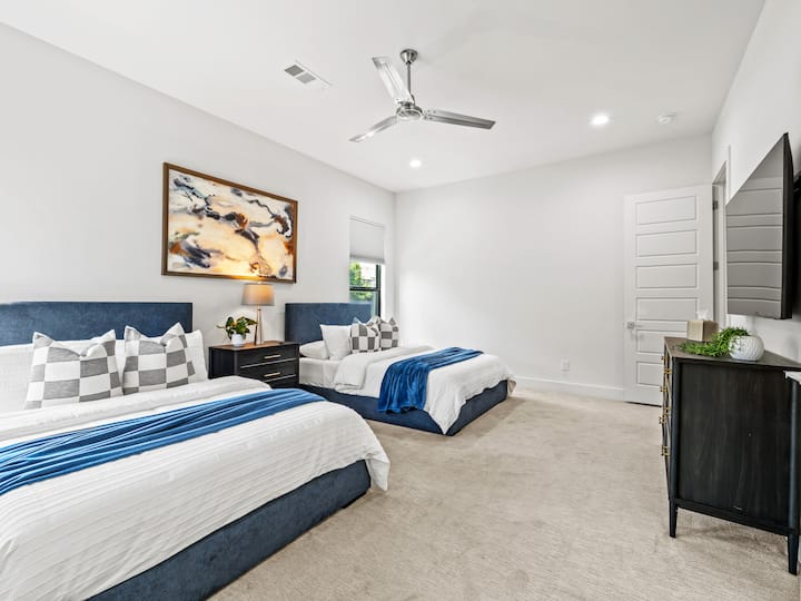 Spacious room with 2 plush queen beds, navy blue headboards & crisp white linens — sleeps 4 comfortably. Private en-suite bathroom, ceiling fan & hotel-quality framed art.