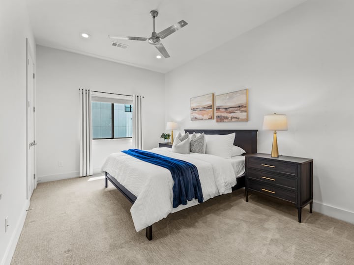 King bed with plush white linens, navy throw & charcoal upholstered headboard — your private retreat for a great night's sleep. Ceiling fan, soft lighting & serene décor included.