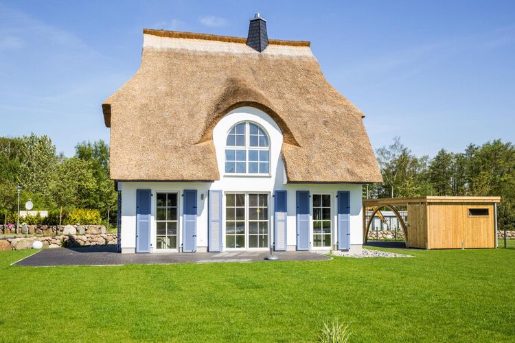 A newly constructed house features a thatched roof and large windows, allowing natural light to fill the interior. The exterior is complemented by a well-maintained lawn and nearby wooden structure, creating a serene and inviting environment.