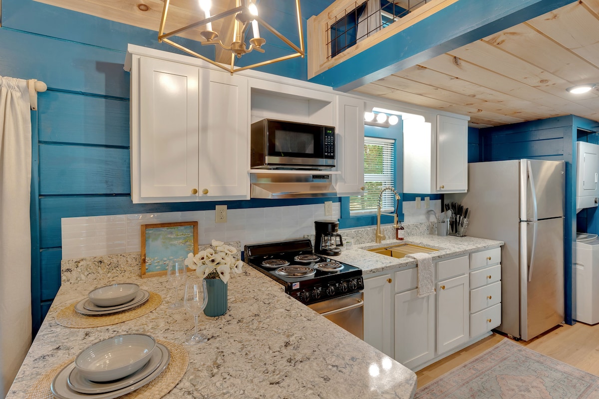 An open kitchen area features white cabinets and a granite countertop with a sink and stove. Modern appliances, including a microwave and refrigerator, are visible. A dining counter with seating for four is located in the foreground, enhancing the functional layout of the space.