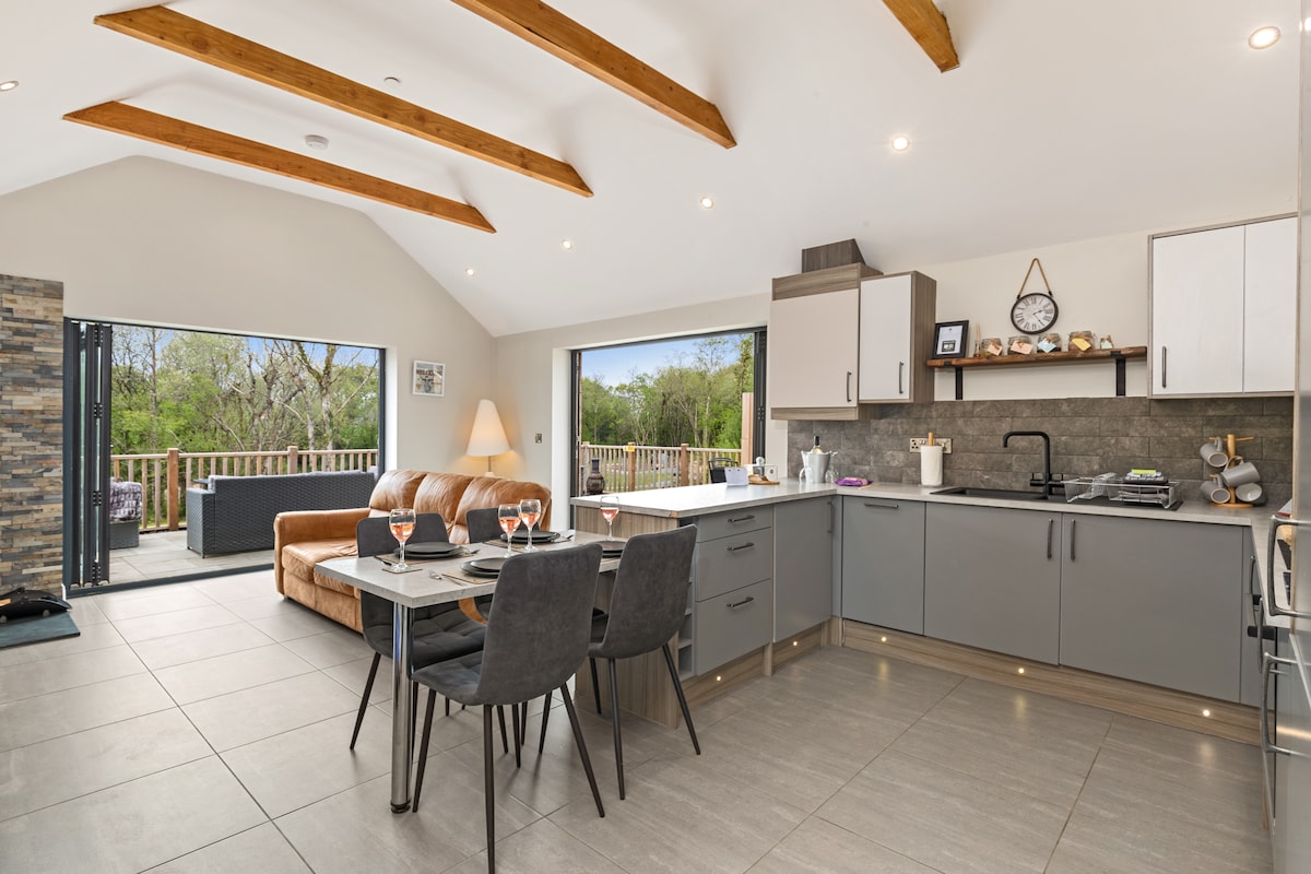 An open-plan living area features sleek cabinetry and modern appliances in a well-equipped kitchen. A dining table with chairs is set, while a comfortable sofa sits nearby. Large glass doors provide access to a terrace, allowing natural light to fill the space.