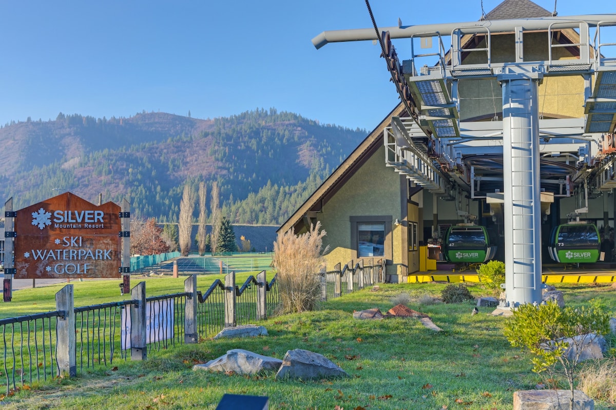 The outdoor area showcases a gondola lift at Silver Mountain Resort, surrounded by lush green grass and majestic mountains in the background. A wooden sign indicating 'Ski, Waterpark, Golf' is prominently displayed, offering a glimpse of the resort's varied activities.