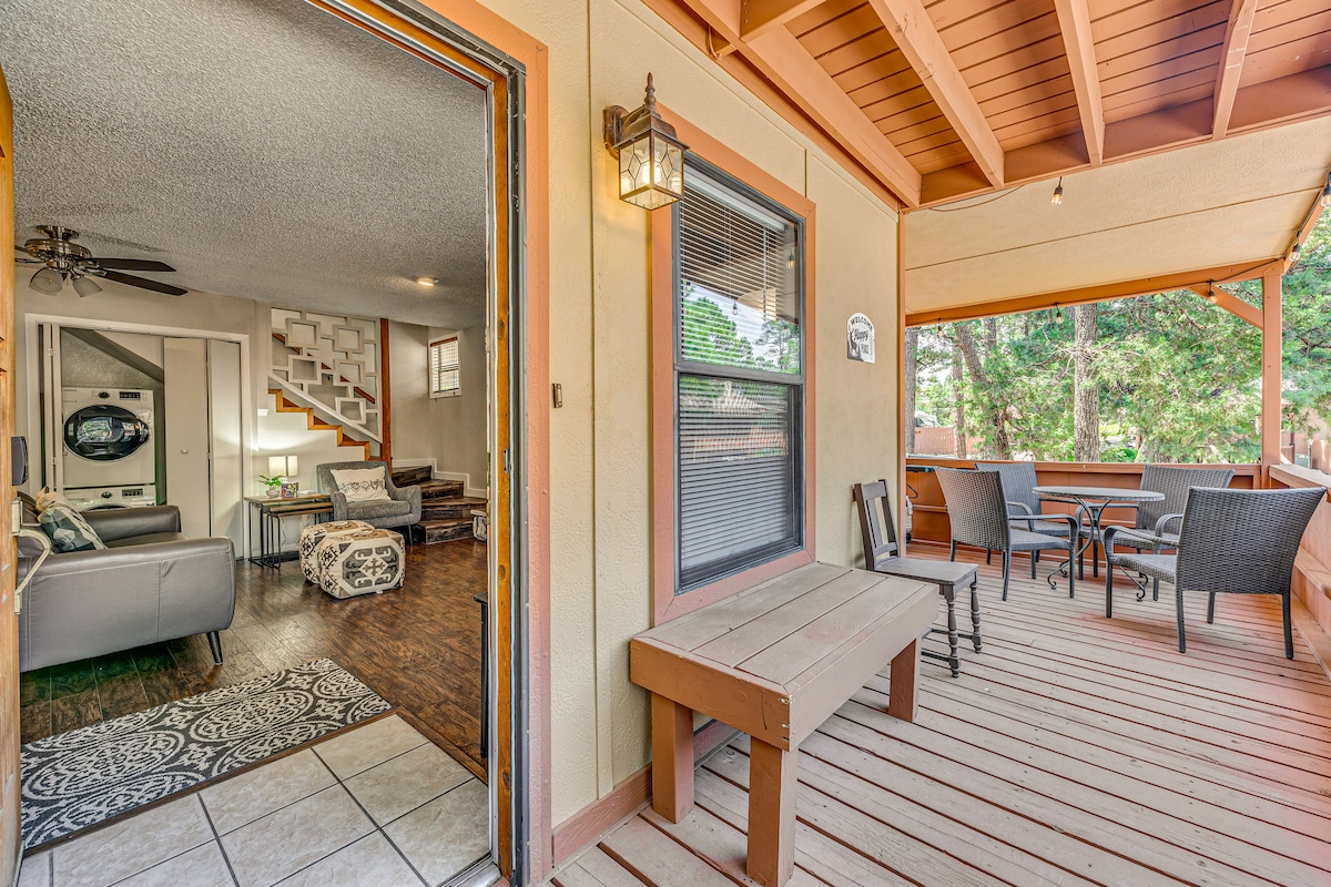An inviting entryway leads to a spacious deck area, featuring a wooden bench and several chairs. The doorway provides a view of the interior living space, which is adorned with comfortable seating and decorative elements, while natural light streams in from the nearby windows.