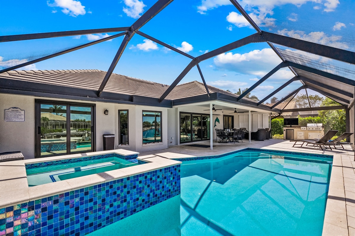 A spacious outdoor area features a large pool surrounded by a screened enclosure. A hot tub is adjacent to the pool, alongside comfortable loungers. Multiple sliding glass doors lead to the interior living space, providing access to the serene views of the canal.
