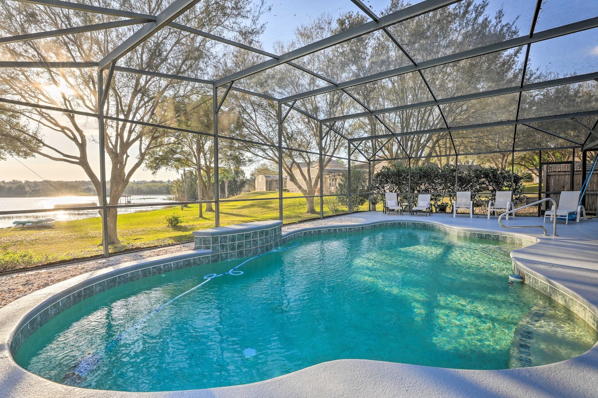 A screened lanai encapsulates a private pool, featuring a gentle curve and a refreshing blue hue. Sunlight reflects off the water surface. Surrounding the pool are views of green grass and trees, along with lounge chairs for relaxation and enjoyment.