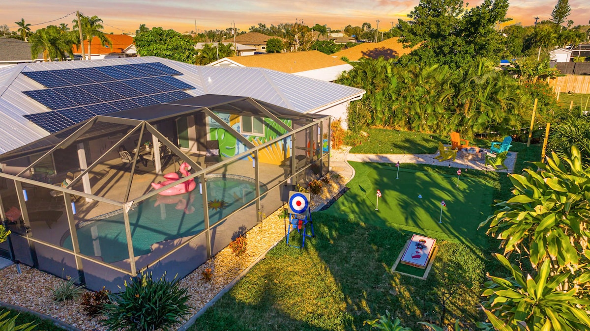 An expansive backyard features a screened-in lanai with a heated pool and colorful inflatables. A golf putting green and cornhole setup are visible, surrounded by landscaped lawns and palm trees. Solar panels adorn the roof, and vibrant outdoor seating areas invite relaxation.
